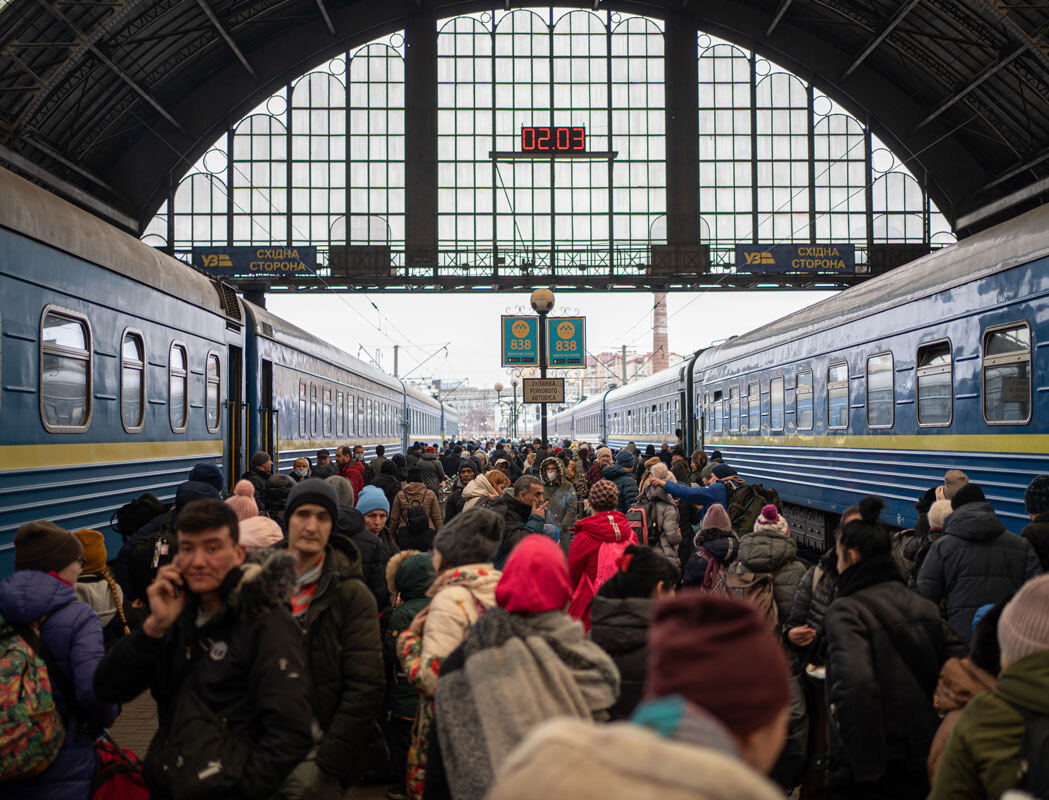 Eine Menschenwenge steht auf einem Bahnhofsgleis zwischen zwei Zügen.