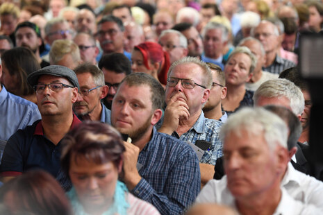 Männer und Frauen sitzen in einem Saal.