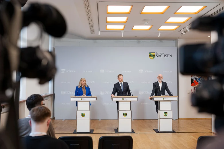 Drei Menschen stehen hinter Rednerpulten.