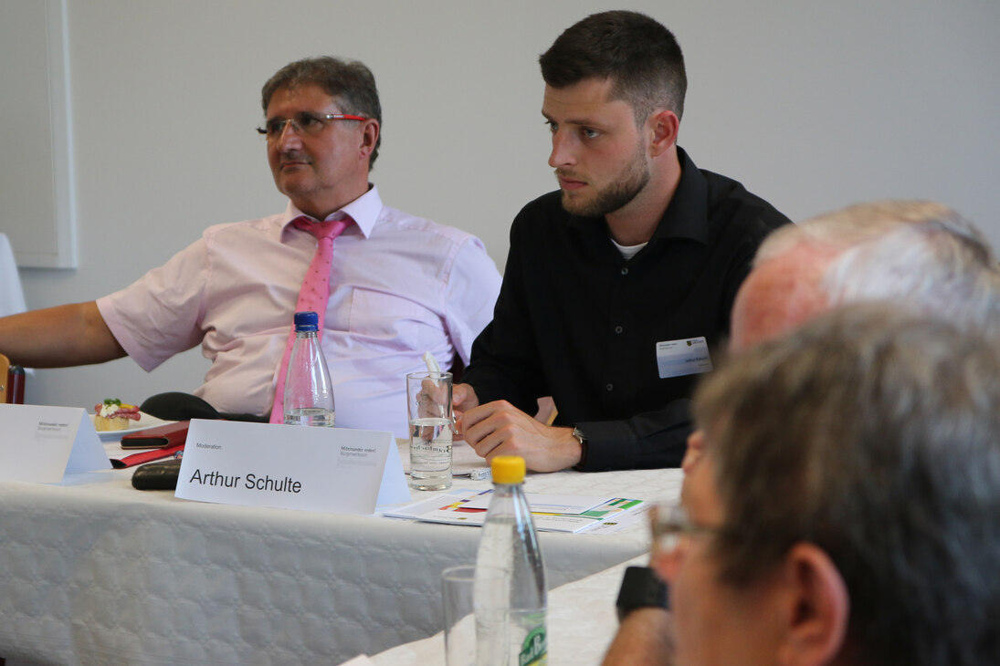 Mehrere Menschen sitzen an einem Tisch und diskutieren.