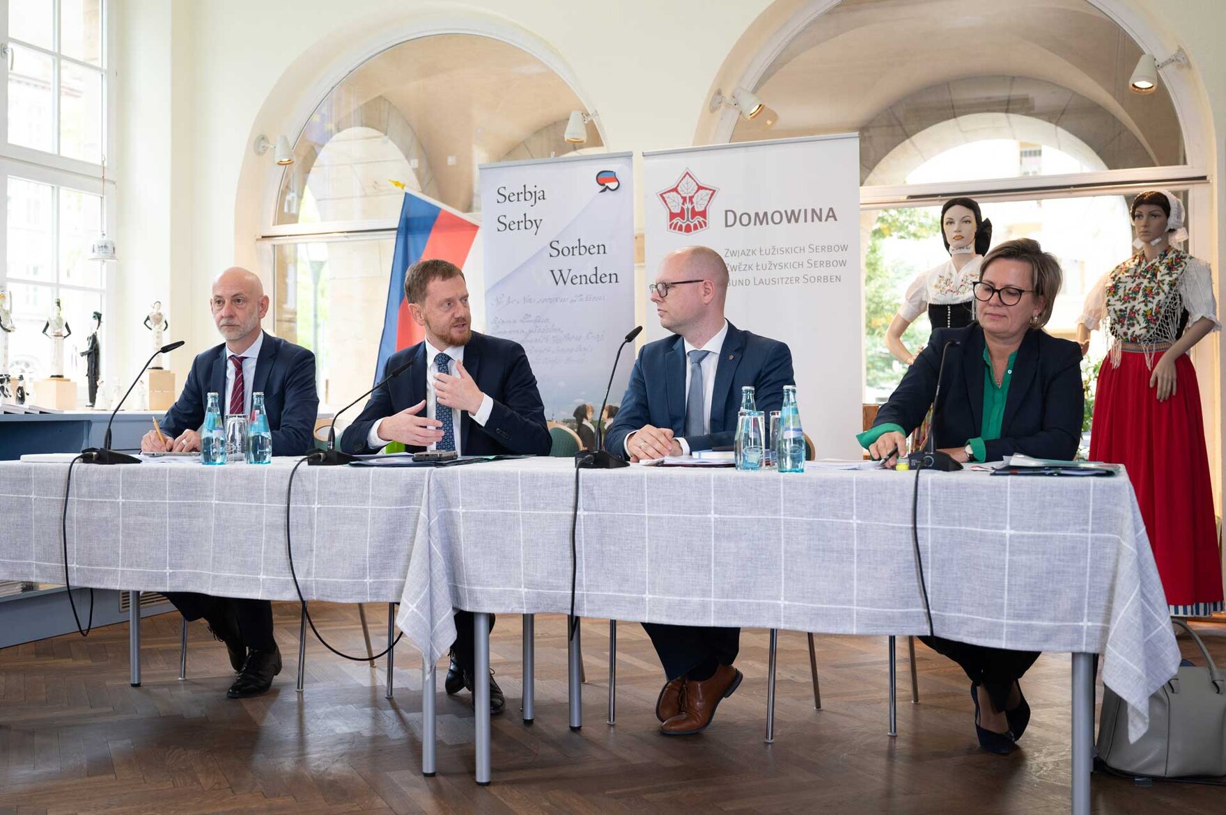 Vier Personen sitzen an einem Tisch und halten eine Pressekonferenz.