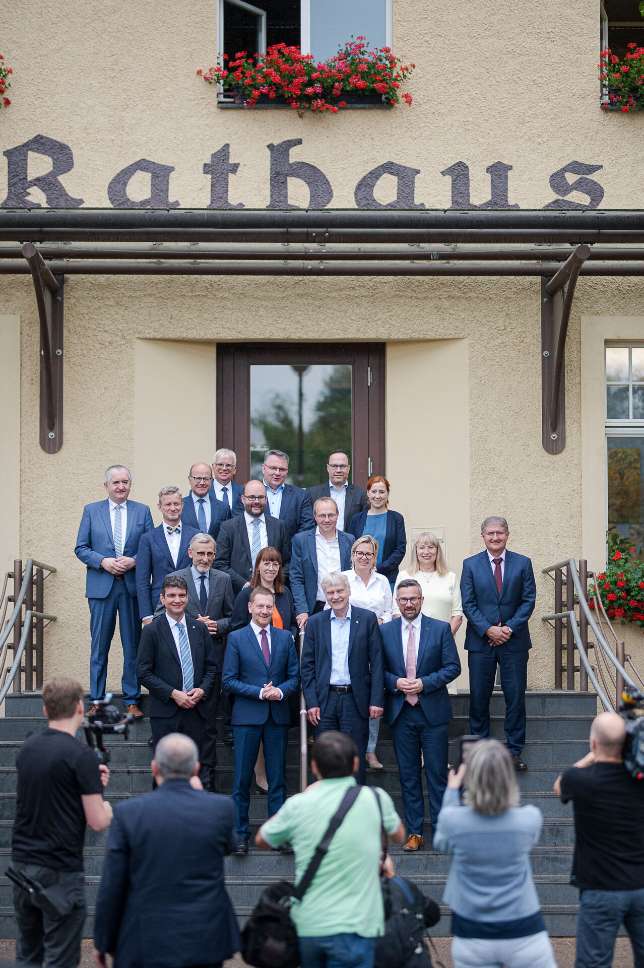 Männer und Frauen stehen auf einer Treppe. Vor ihnen stehen Fotografen.