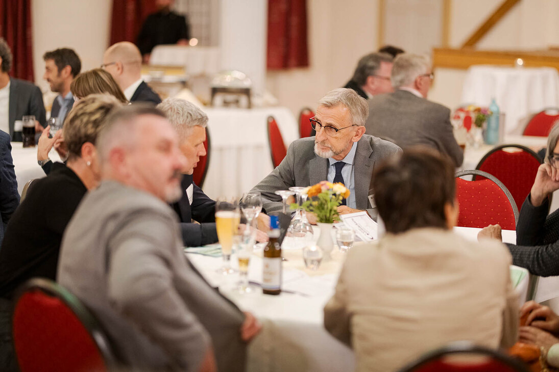 Männer und Frauen unterhalten sich an einem Tisch in einem großen Saal.