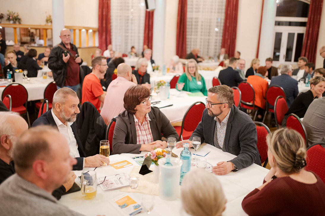 Männer und Frauen unterhalten sich an einem Tisch in einem großen Saal.