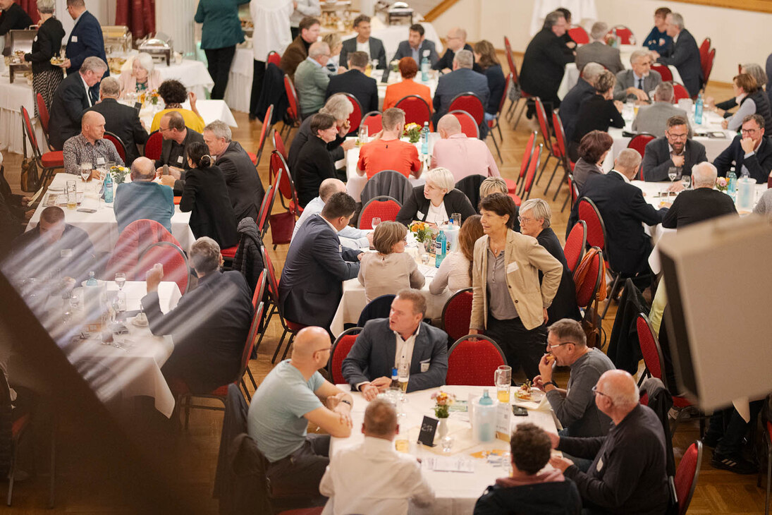 Männer und Frauen unterhalten sich an einem Tisch in einem großen Saal.