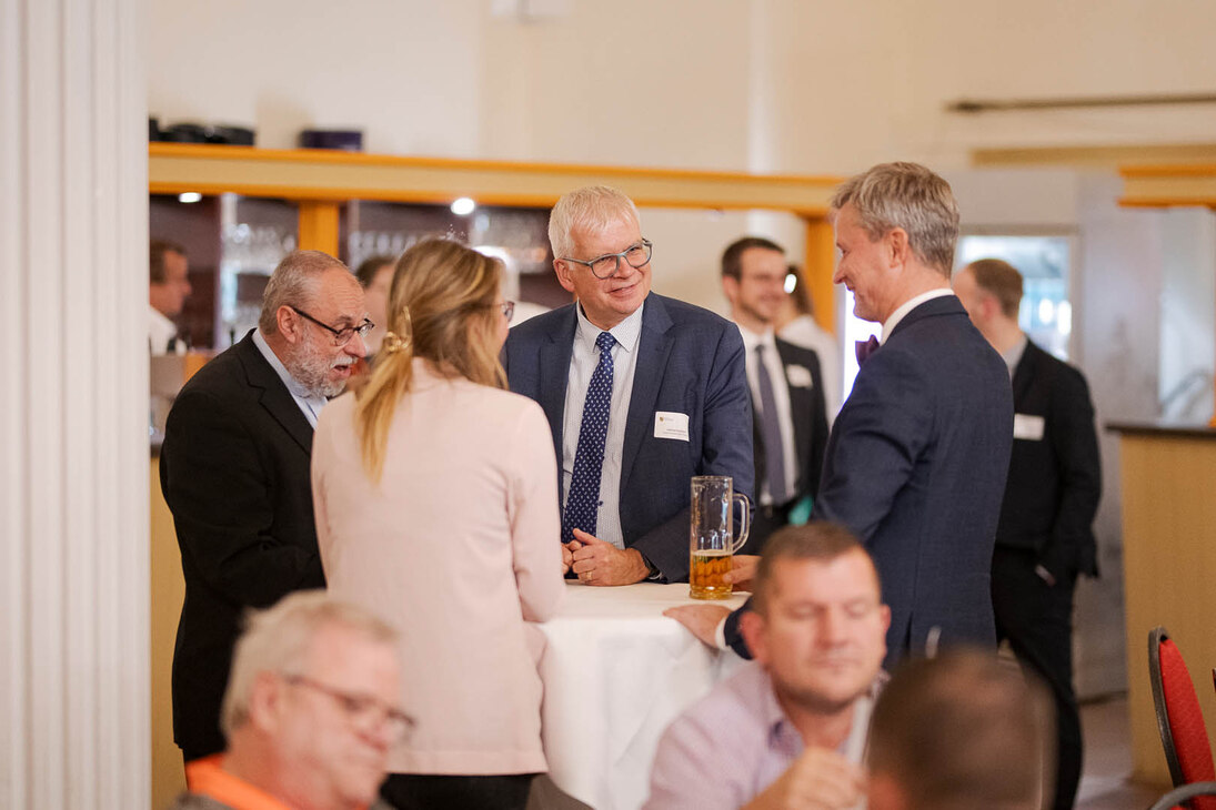 Männer und Frauen unterhalten sich an einem Tisch in einem großen Saal.