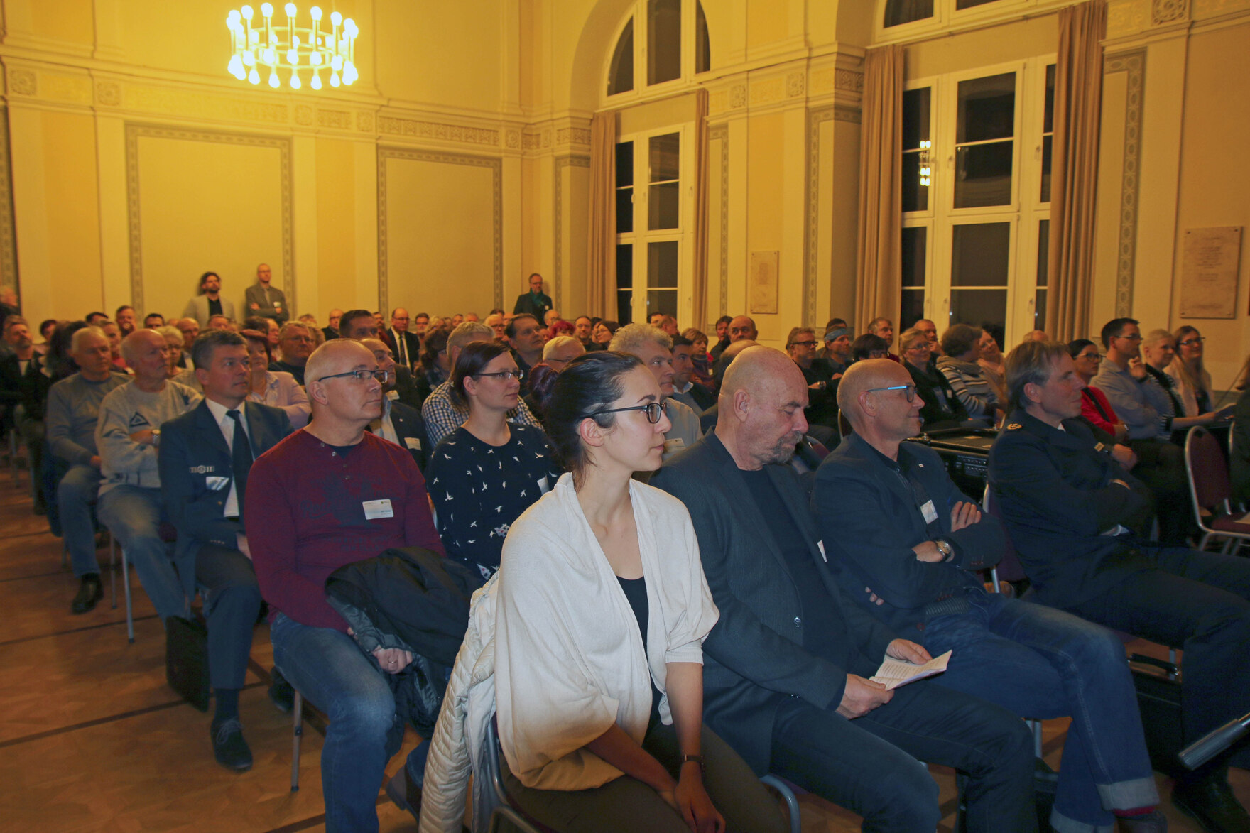 Männer und Frauen sitzen in einem großen Saal.