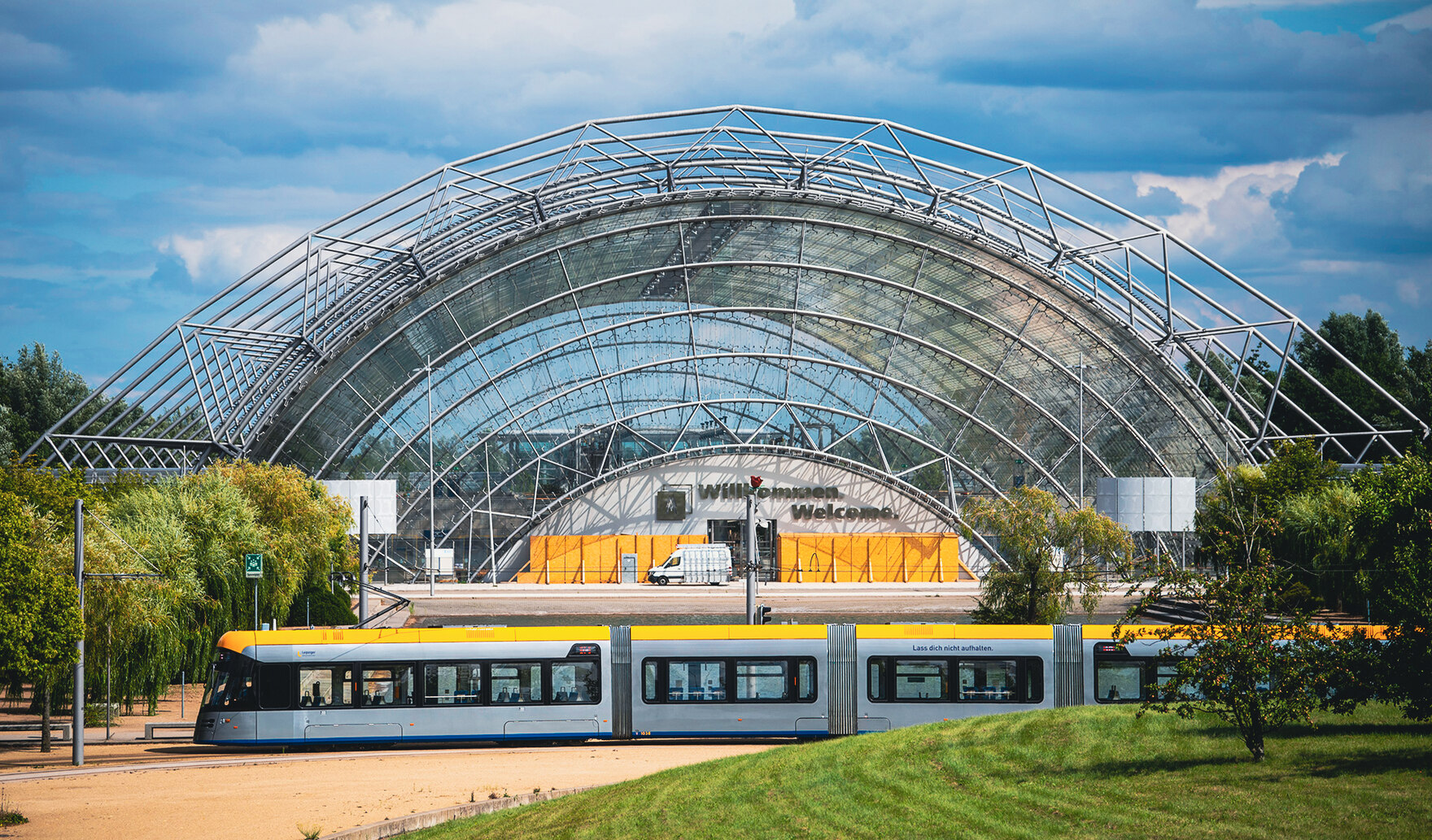 Eine Straßenbahn fährt an einem großen Gebäude mit Glasdach vorbei.