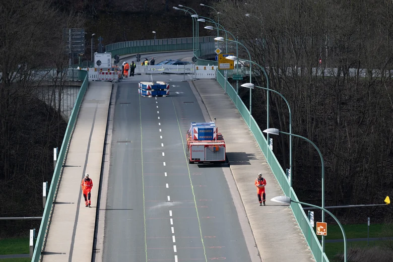 Zwei Männer und ein Schwerlastauto stehen auf einer Brücke.