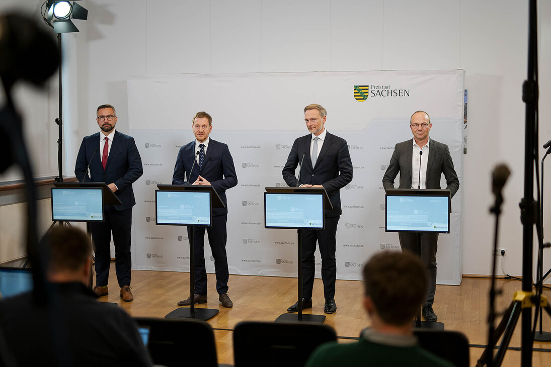 Vier Männer halten an Stehpulten eine Pressekonferenz.