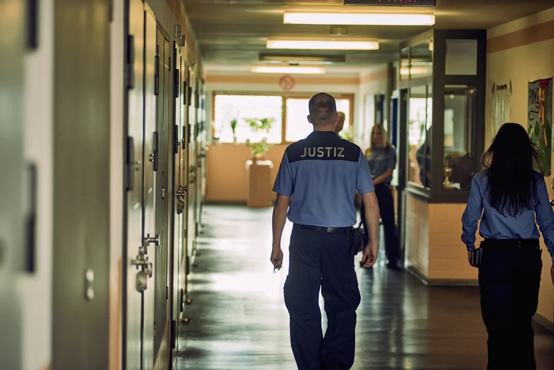 Ein Justizbeamter und eine Justizbeamtin laufen nebeneinander auf einem Gang in einem Gefängnis.