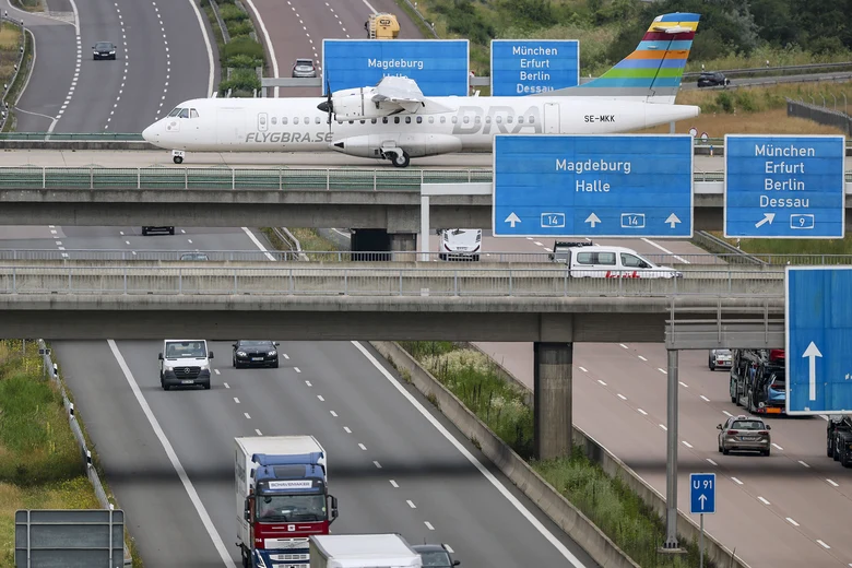 Ein Flugzeug fährt über eine Rollbahn. Die Rollbahn verläuft über einer Autobahn, auf der Autos entlang fahren.