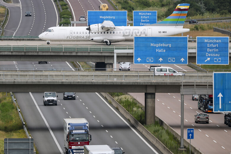 Ein Flugzeug fährt über eine Rollbahn. Die Rollbahn verläuft über einer Autobahn, auf der Autos entlang fahren.