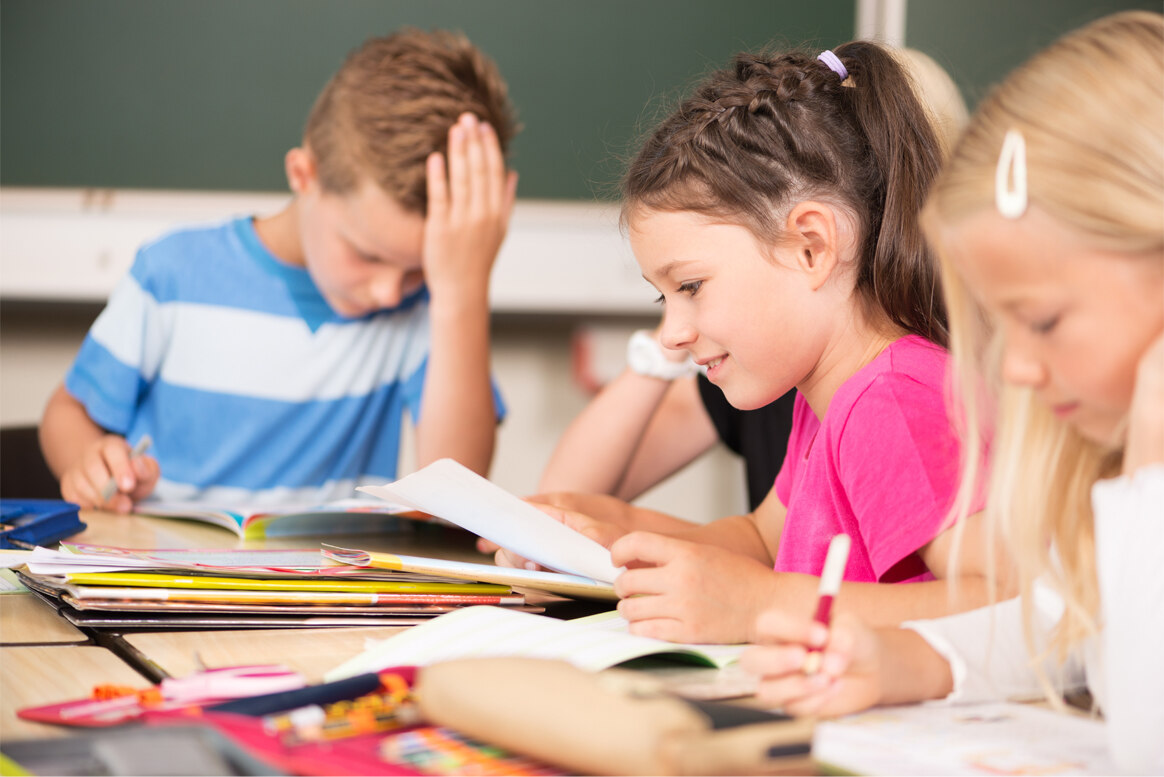 Kinder sitzen an einer Schulbank.