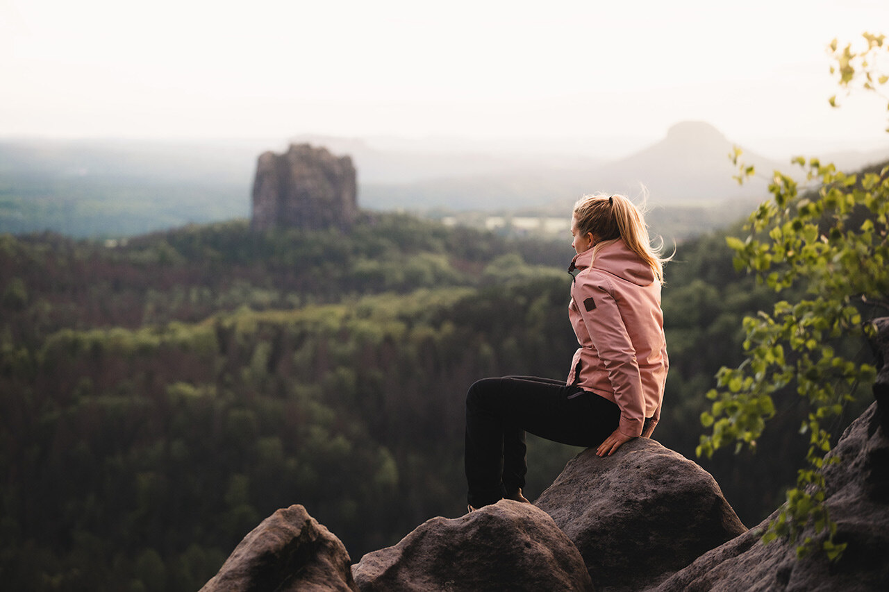 Eine Frau sitzt auf einem Felsen und blickt auf weitere Felsen.