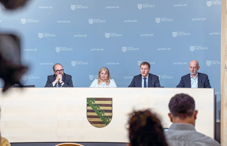 Männer und Frauen sitzen auf einem Podium.