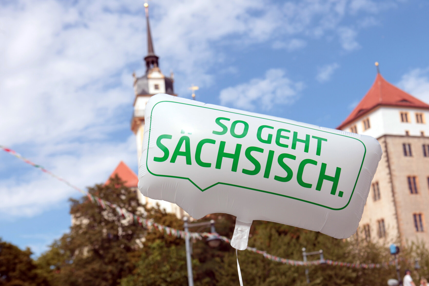 Ein Luftballon mit der Aufschrift So geht Sächsisch. Im Hintergrund steht ein Schloss.