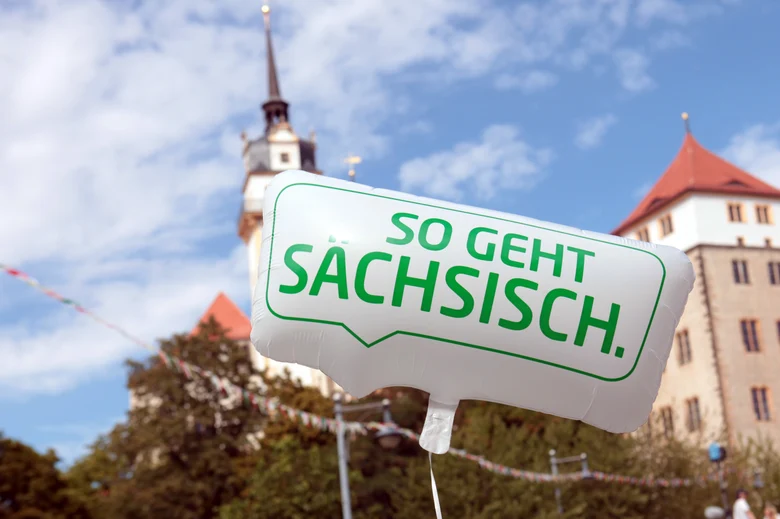Ein Luftballon mit der Aufschrift So geht Sächsisch. Im Hintergrund steht ein Schloss.