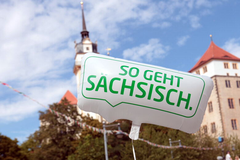 Ein Luftballon mit der Aufschrift So geht Sächsisch. Im Hintergrund steht ein Schloss.