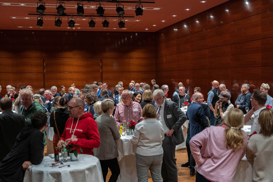 In einem Saal stehen Stehtische an den viele Menschen stehen.