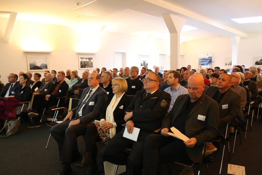 Männer und Frauen sitzen in einem großen Saal.
